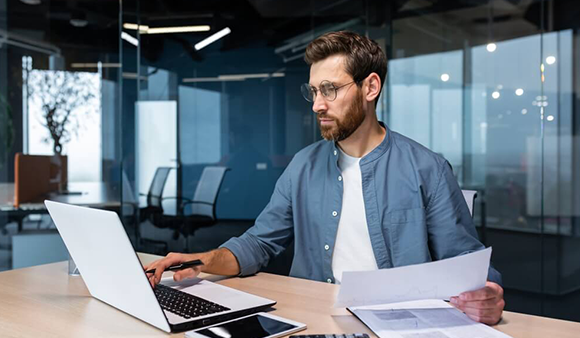 man holding papers working on laptop