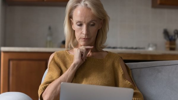 older woman sat thinking looking down at laptop