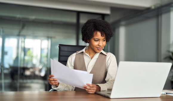 Professional busy young African American business woman account manager executive checking document financial report using laptop checking file working with enterprise software sitting at office desk.